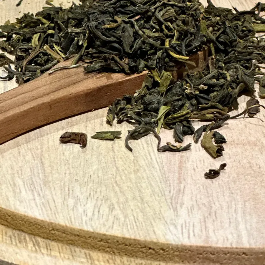 Loose green tea leaves on a wooden scoop